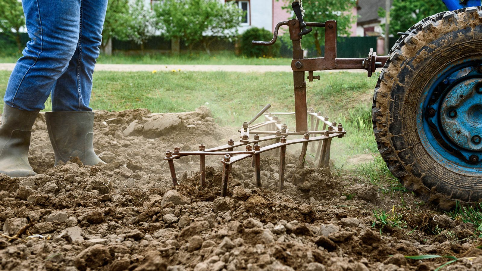 A gardener wearing black boots, using a machine, tilling the soil in a garden.